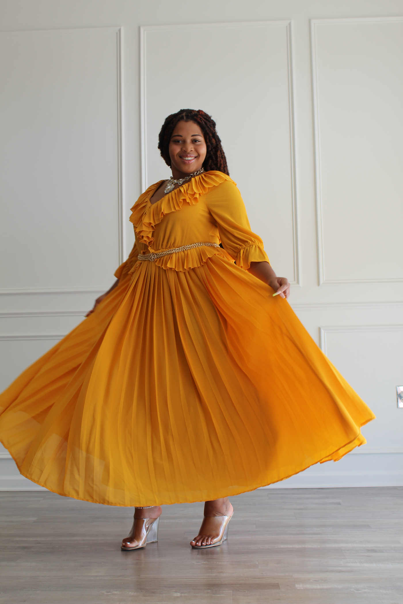 A sweet dress that features a pleated flounce v neck and 3/4 bell sleeves. A darted bodice, peplum detail at the waist that is accessorized with a gold-tone chain layered belt, atop a flowy maxi skirt. 